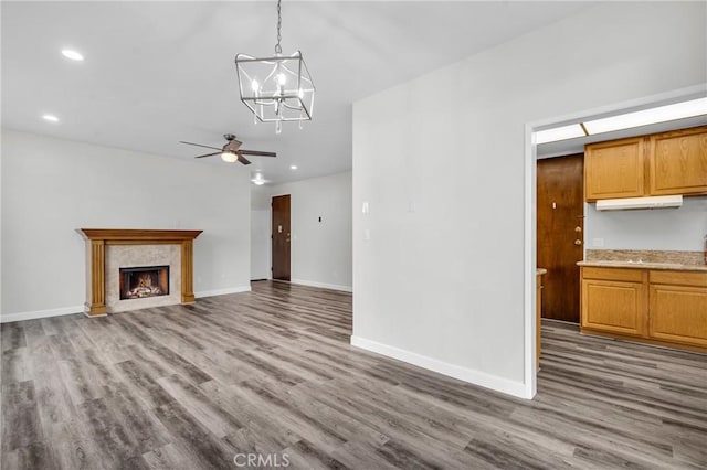 unfurnished living room featuring hardwood / wood-style flooring, ceiling fan with notable chandelier, and a fireplace