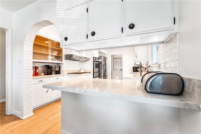 kitchen with backsplash, white cabinets, light wood-type flooring, kitchen peninsula, and stainless steel appliances