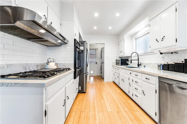 kitchen featuring white cabinetry, sink, washer / clothes dryer, appliances with stainless steel finishes, and light wood-type flooring