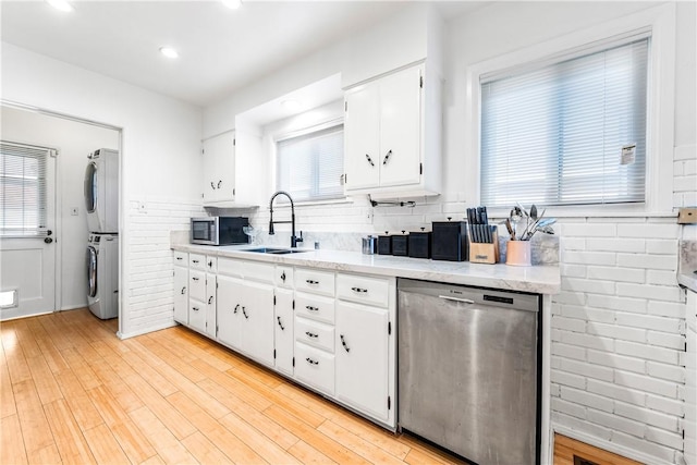 kitchen featuring appliances with stainless steel finishes, light wood-type flooring, stacked washing maching and dryer, sink, and white cabinetry