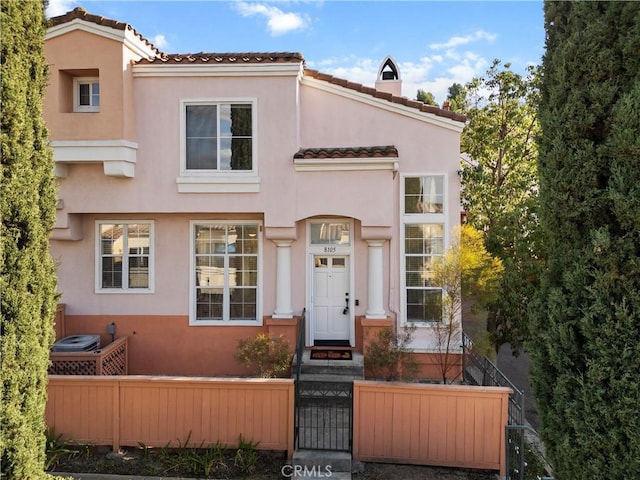 mediterranean / spanish-style house featuring a tiled roof, a fenced front yard, and stucco siding