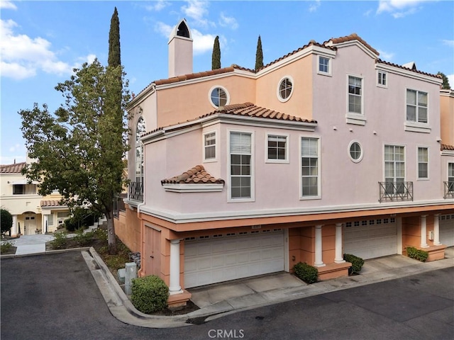 mediterranean / spanish-style house with a garage, a chimney, and stucco siding