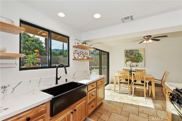 kitchen with ceiling fan, light stone countertops, sink, and range with gas cooktop