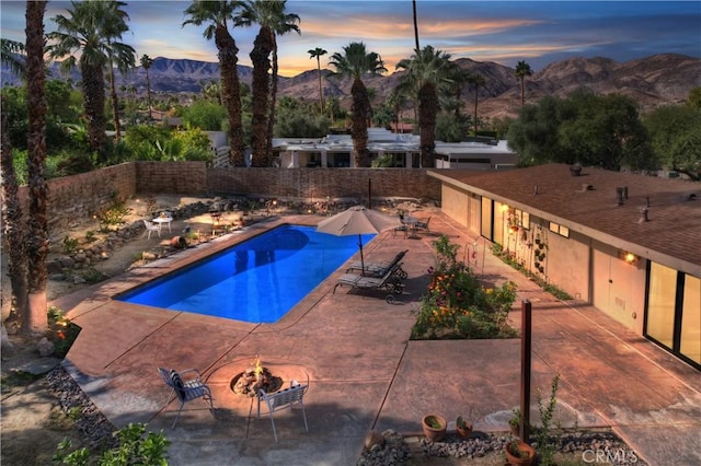 pool at dusk with a mountain view, a patio area, and an outdoor fire pit