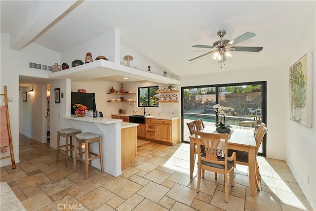 kitchen featuring sink, vaulted ceiling, ceiling fan, a kitchen bar, and kitchen peninsula