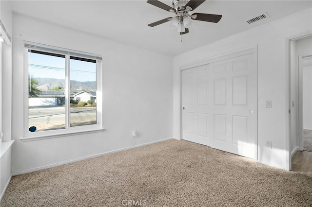 unfurnished bedroom featuring a mountain view, carpet flooring, and ceiling fan