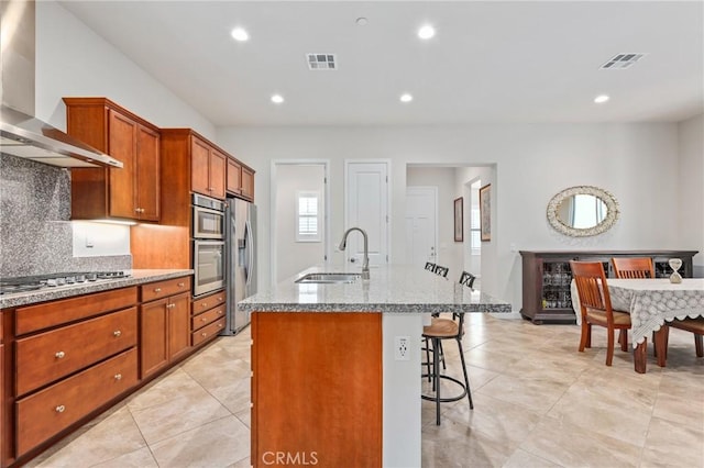 kitchen with stainless steel appliances, a sink, a kitchen breakfast bar, wall chimney range hood, and a center island with sink