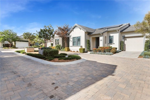 single story home featuring a garage, driveway, roof mounted solar panels, and stucco siding