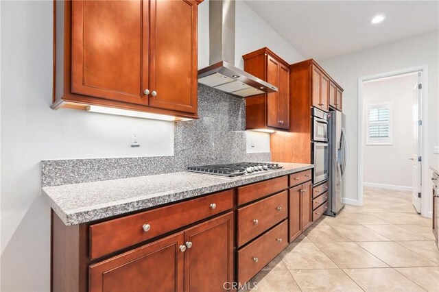 kitchen with decorative backsplash, appliances with stainless steel finishes, light stone counters, wall chimney range hood, and light tile patterned flooring