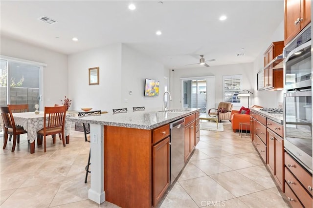 kitchen with stainless steel appliances, visible vents, open floor plan, a sink, and an island with sink