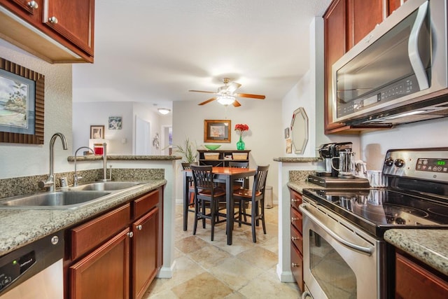 kitchen featuring light stone counters, ceiling fan, stainless steel appliances, and sink