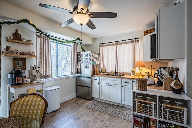 kitchen with white cabinets, sink, ceiling fan, stainless steel fridge, and light wood-type flooring