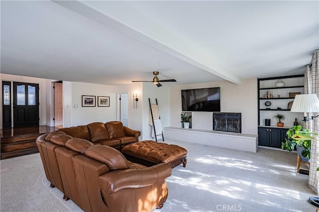 carpeted living room with a fireplace, beam ceiling, and ceiling fan