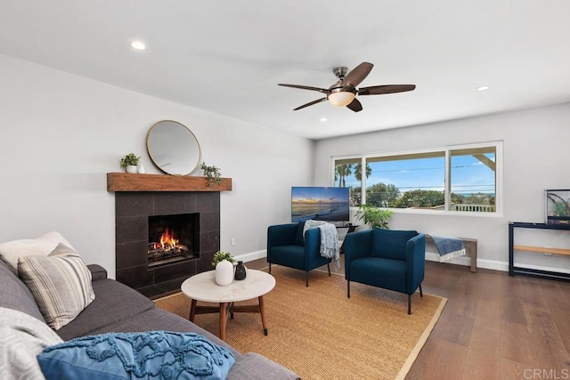 living room featuring a tiled fireplace, ceiling fan, and dark hardwood / wood-style floors