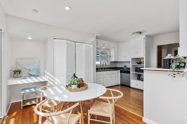 kitchen with stainless steel dishwasher, white cabinetry, sink, and hardwood / wood-style floors