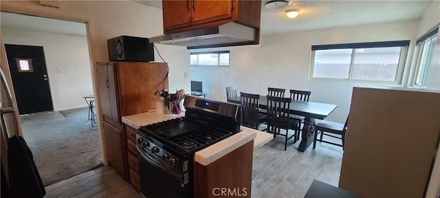 kitchen featuring light wood-type flooring, wall chimney exhaust hood, and stainless steel range with gas stovetop