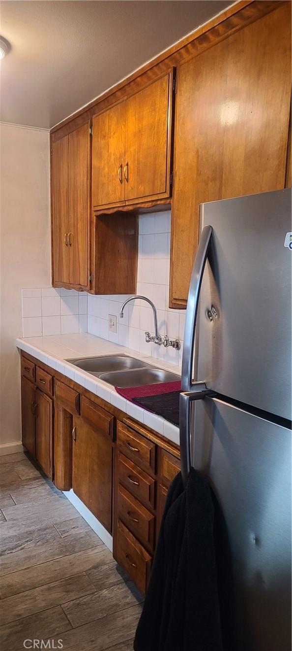 kitchen with decorative backsplash, sink, tile countertops, stainless steel refrigerator, and hardwood / wood-style flooring