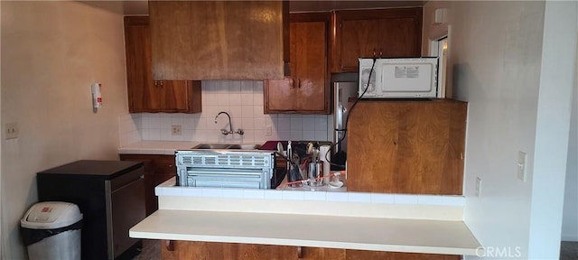 kitchen with sink, stainless steel refrigerator, kitchen peninsula, and tasteful backsplash