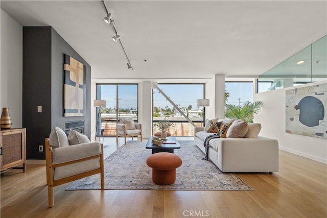 living room featuring a glass covered fireplace, rail lighting, wood finished floors, and baseboards