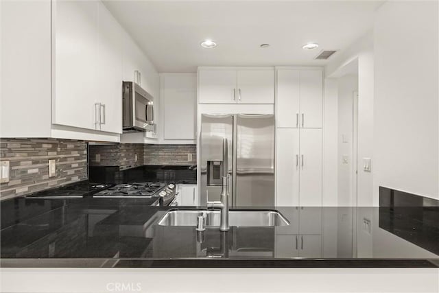 kitchen featuring sink, tasteful backsplash, kitchen peninsula, white cabinets, and appliances with stainless steel finishes