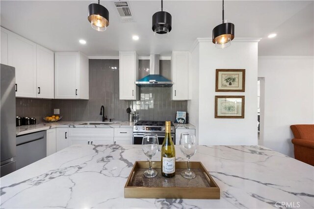 kitchen featuring appliances with stainless steel finishes, hanging light fixtures, wall chimney range hood, white cabinets, and sink