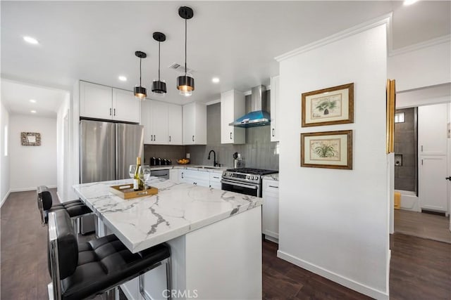 kitchen featuring a sink, light stone counters, dark wood finished floors, stainless steel appliances, and wall chimney range hood