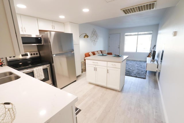 kitchen with appliances with stainless steel finishes, white cabinetry, sink, and light hardwood / wood-style floors