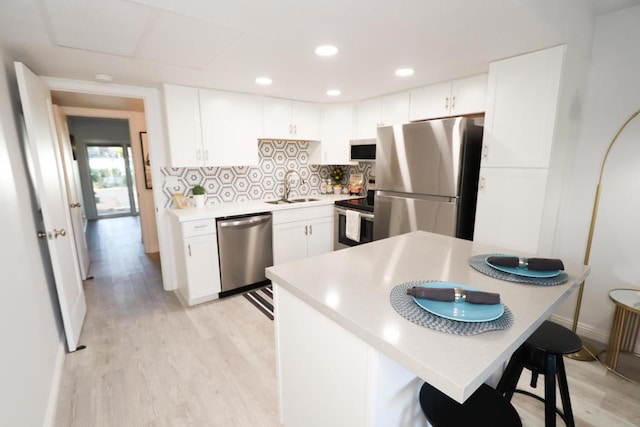 kitchen with stainless steel appliances, sink, white cabinets, a kitchen breakfast bar, and tasteful backsplash