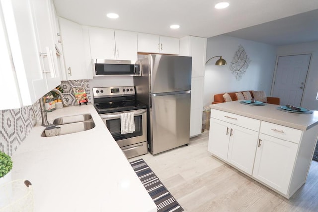 kitchen featuring appliances with stainless steel finishes, white cabinetry, light wood-type flooring, and sink