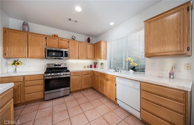 kitchen with sink, tile counters, light tile patterned flooring, and appliances with stainless steel finishes