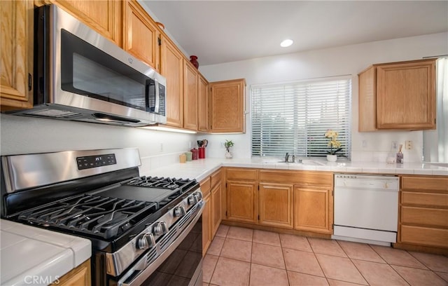 kitchen with stainless steel appliances, light tile patterned flooring, sink, and tile countertops