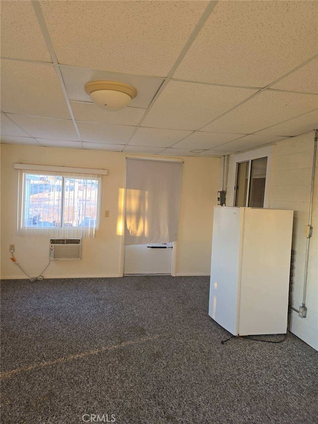 unfurnished room with dark colored carpet, a drop ceiling, and a wall mounted AC