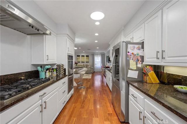 kitchen featuring white cabinets, dark stone countertops, light hardwood / wood-style floors, stainless steel appliances, and extractor fan