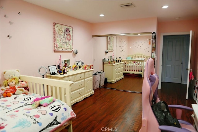 bedroom with dark hardwood / wood-style flooring, a nursery area, and a closet