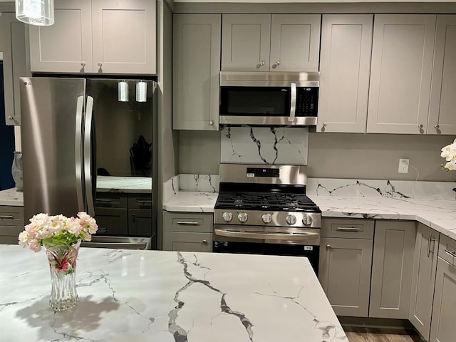 kitchen with gray cabinets, light stone countertops, hardwood / wood-style floors, and appliances with stainless steel finishes