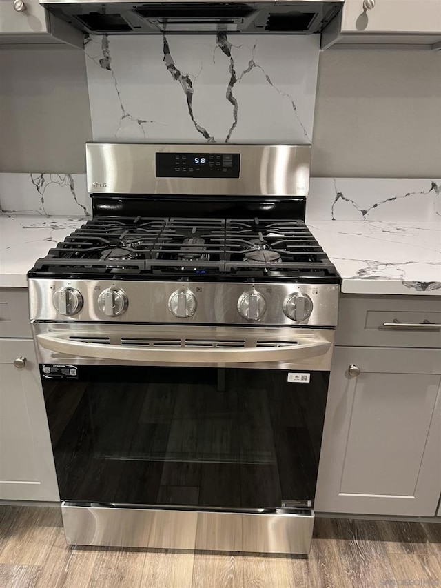 kitchen with dark hardwood / wood-style flooring, stainless steel gas stove, and light stone counters