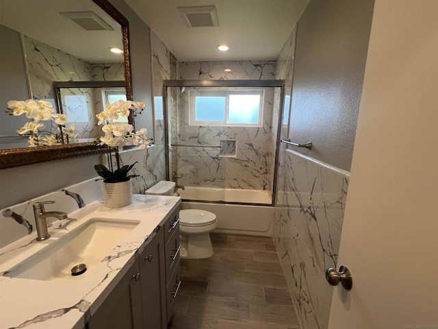 full bathroom with shower / bath combination with glass door, vanity, hardwood / wood-style flooring, and toilet