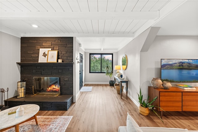 living room with beamed ceiling, a stone fireplace, and light hardwood / wood-style flooring