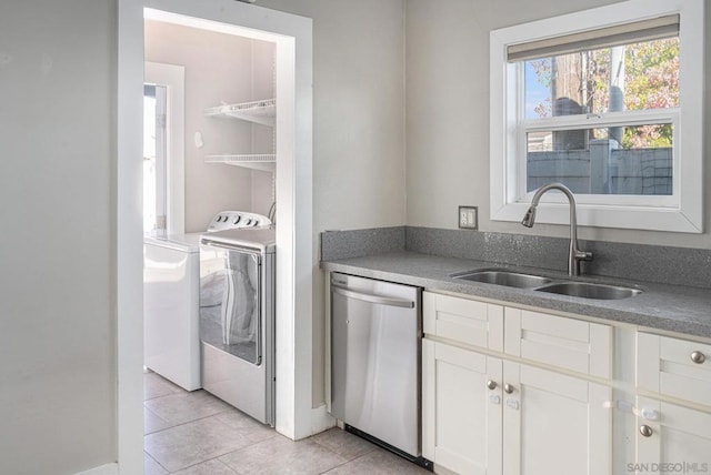 kitchen with sink, light tile patterned floors, stainless steel dishwasher, washer / clothes dryer, and white cabinets