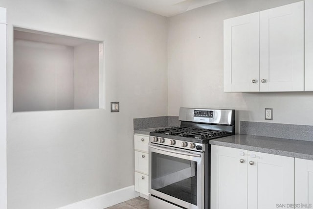 kitchen featuring stainless steel gas range oven, white cabinets, and light tile patterned floors