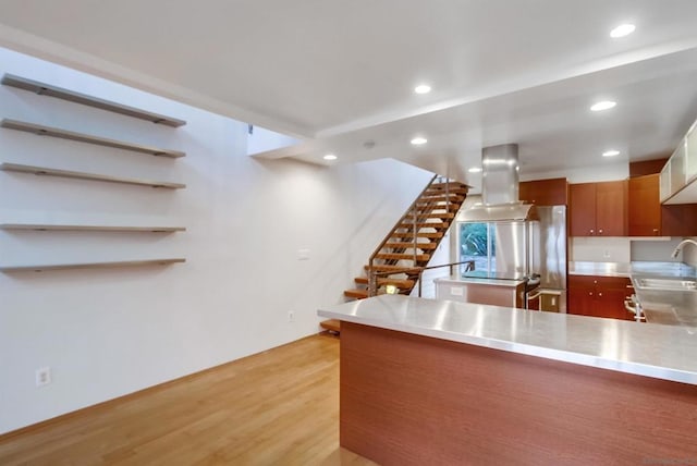 kitchen with kitchen peninsula, island range hood, sink, and light hardwood / wood-style floors