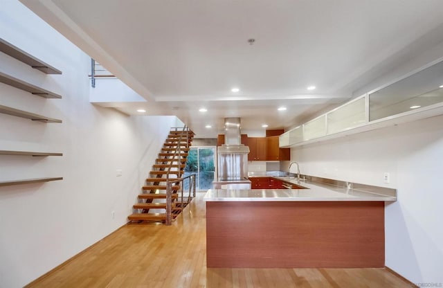 kitchen featuring kitchen peninsula, light wood-type flooring, ventilation hood, and sink