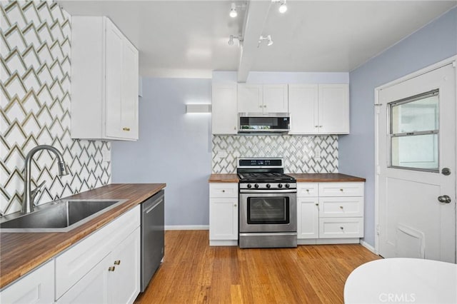 kitchen with wood counters, appliances with stainless steel finishes, white cabinets, and sink