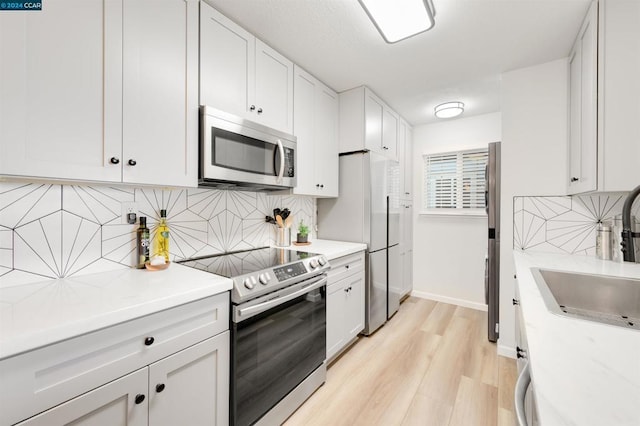 kitchen with backsplash, sink, light wood-type flooring, white cabinetry, and stainless steel appliances