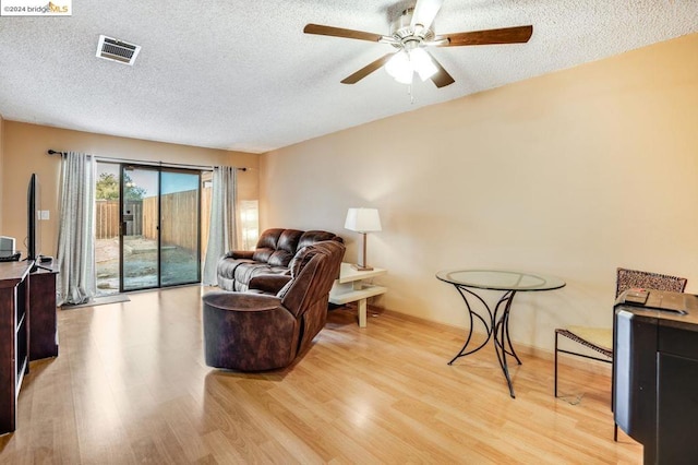 living room with ceiling fan, a textured ceiling, and light hardwood / wood-style flooring