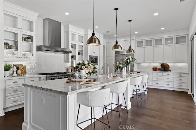 kitchen featuring appliances with stainless steel finishes, wall chimney range hood, a large island with sink, white cabinets, and dark hardwood / wood-style floors