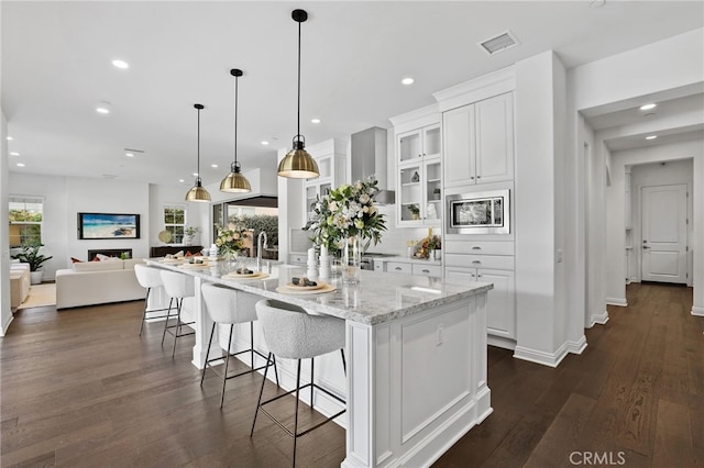 kitchen featuring stainless steel microwave, decorative light fixtures, a large island, dark hardwood / wood-style flooring, and white cabinetry