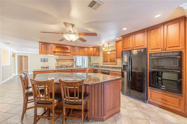 kitchen with a kitchen breakfast bar, a kitchen island with sink, black appliances, pendant lighting, and stone countertops