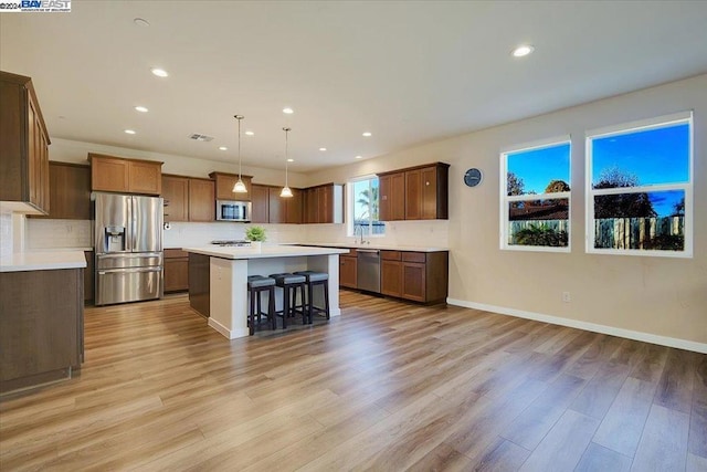 kitchen with a kitchen bar, a center island, stainless steel appliances, and light hardwood / wood-style floors