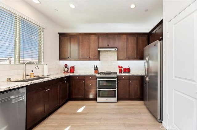 kitchen featuring sink, decorative backsplash, light hardwood / wood-style floors, light stone counters, and stainless steel appliances